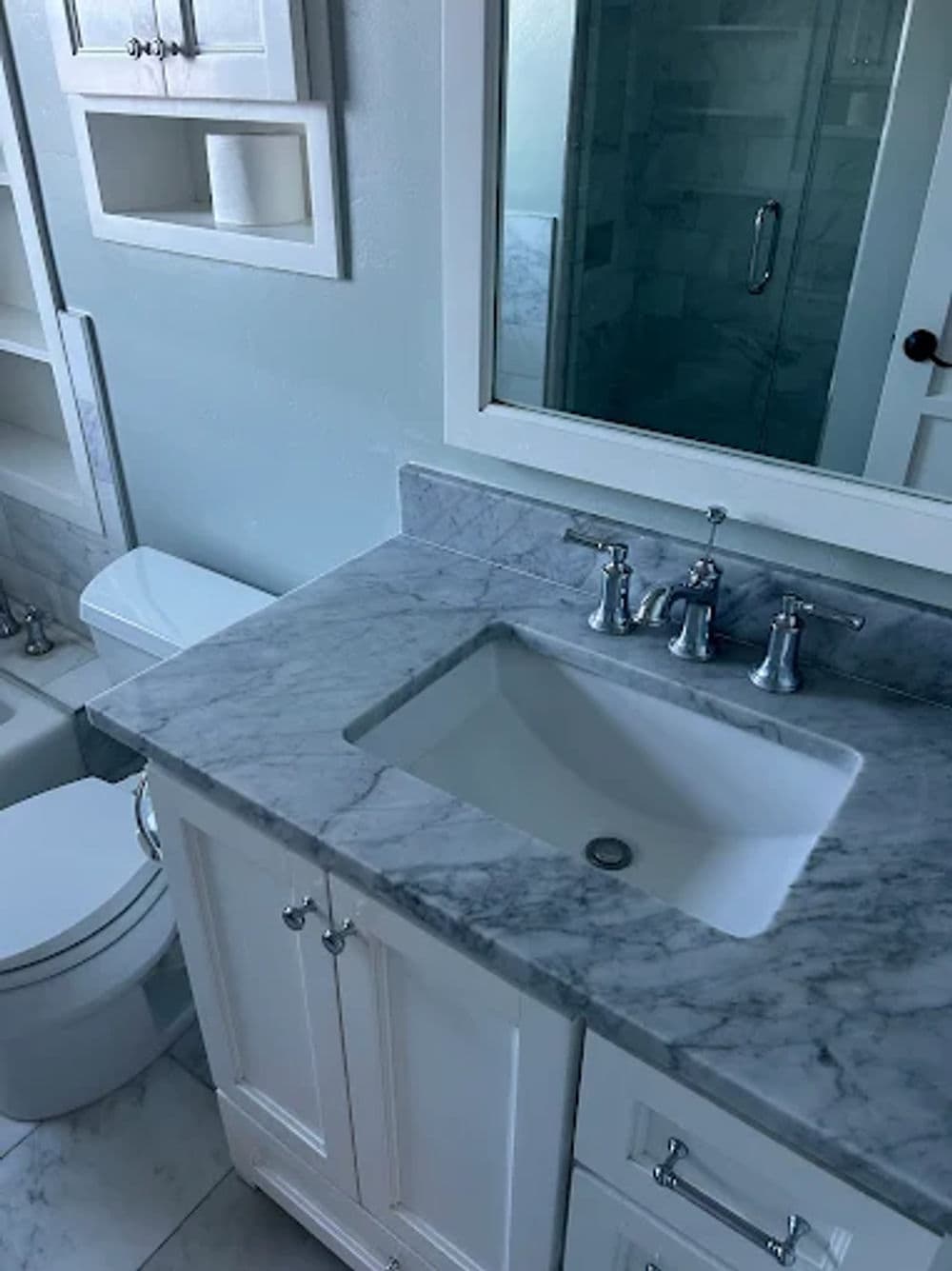Modern bathroom with marble countertop, sink, and clean white cabinetry.